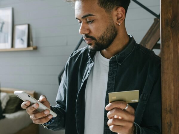 pexels-photo-7620910-7620910 Young man using phone for online shopping at home, holding a credit card.
